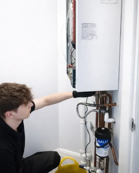 Engineer fitting a magnetic system filter to the pipework beneath a wall mounted boiler