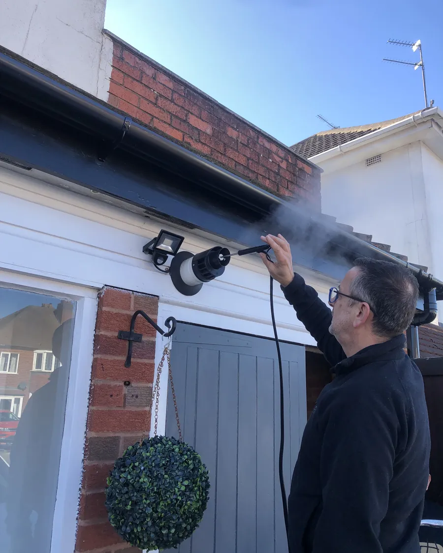 Gas engineer holding an analyser probe into an outside boiler flue terminal during a gas safety inspection