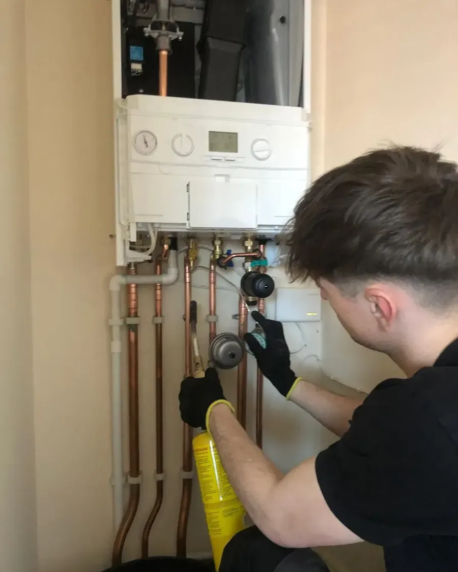 Engineer tightening the copper pipework connections beneath a boiler with a spanner